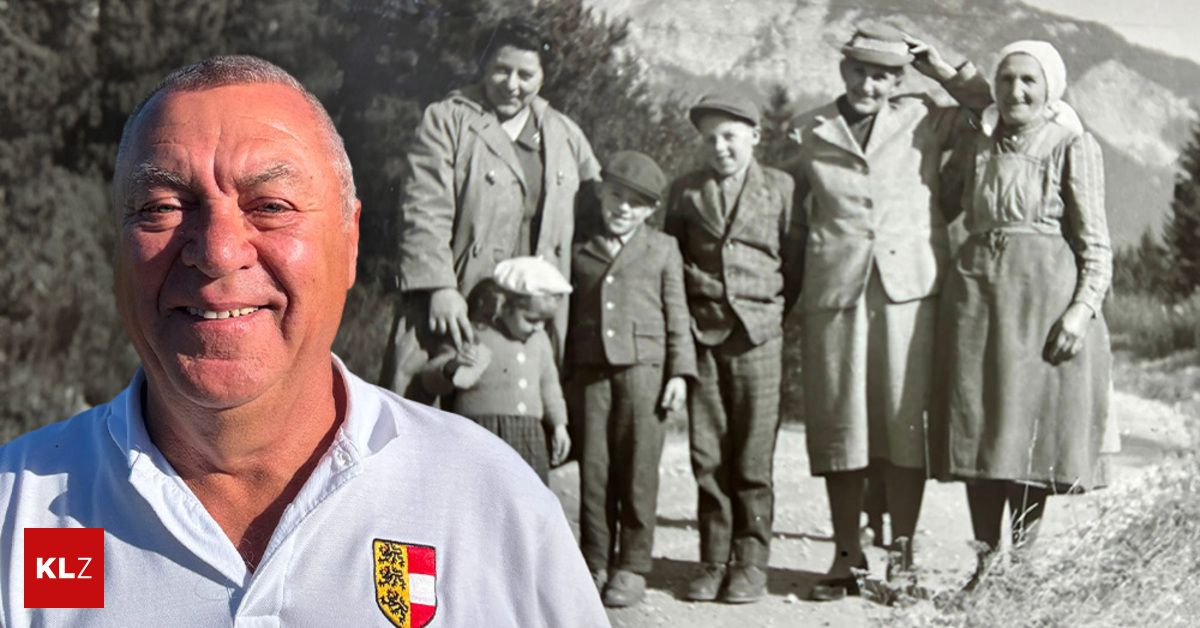 Ein lächelnder Mann in einem weißen Hemd mit einem Wappen steht vor einem schwarz-weißen Familienfoto. Das Familienfoto zeigt eine Frau, die ein Baby hält, einen Jungen in einem Hut und zwei Männer.