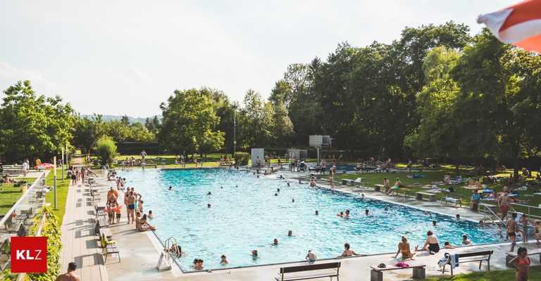 Ein großer Außenpool voller Menschen, die schwimmen und an den Seiten entspannen. Im Hintergrund sind Bäume und Bänke zu sehen.