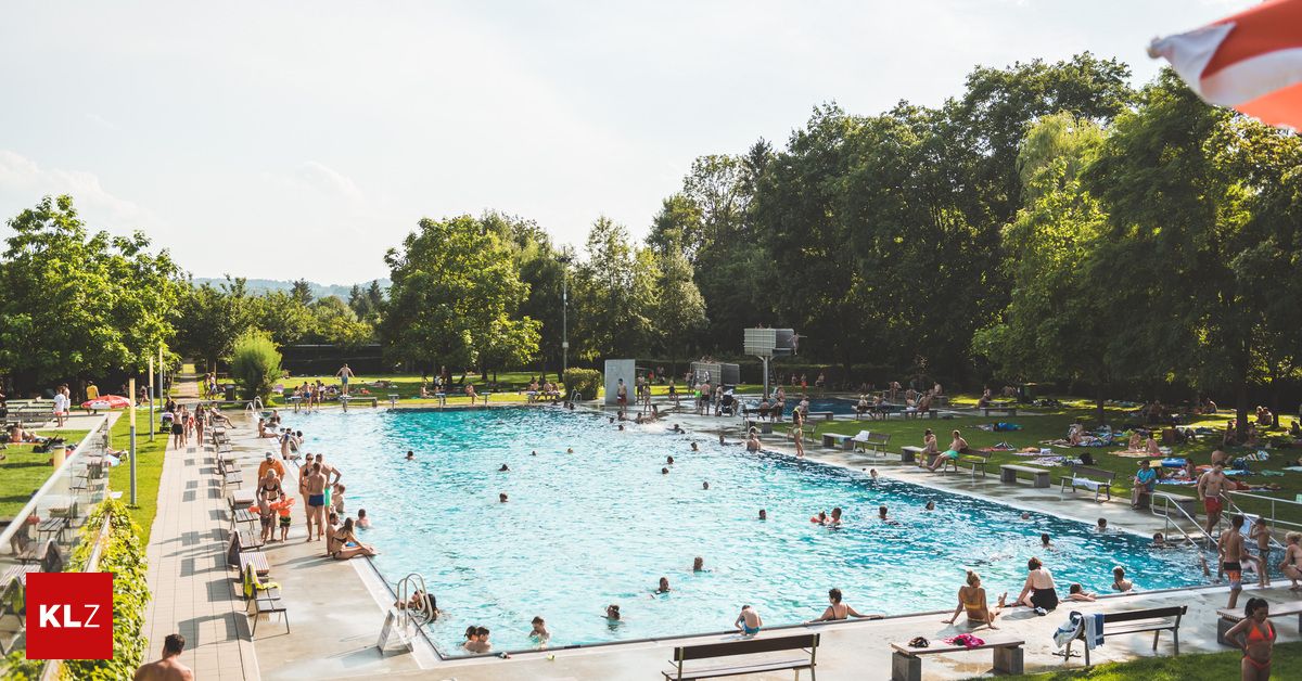 Ein großer Außenpool voller Menschen, die schwimmen und an den Seiten entspannen. Im Hintergrund sind Bäume und Bänke zu sehen.