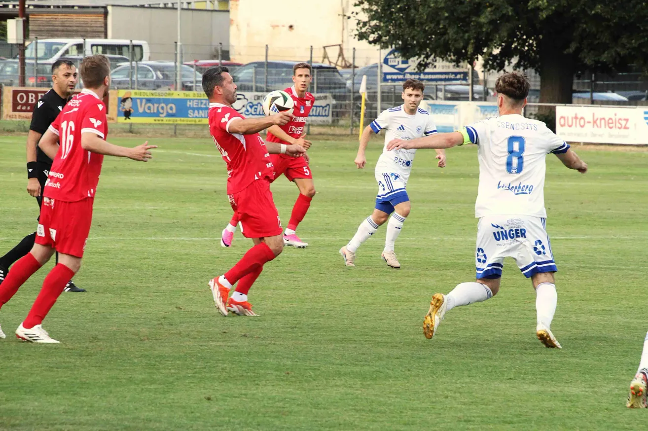 Ein Fußballspiel im Gange, Spieler in roten und weißen Trikots, ein Spieler kurz davor, den Ball zu schießen.