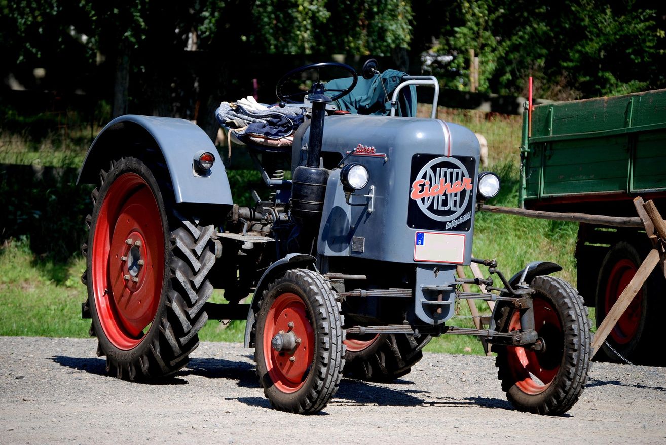 Ein alter Eicher Traktor mit roten Rädern und einem Logo auf der Vorderseite steht auf einem Schotterweg.