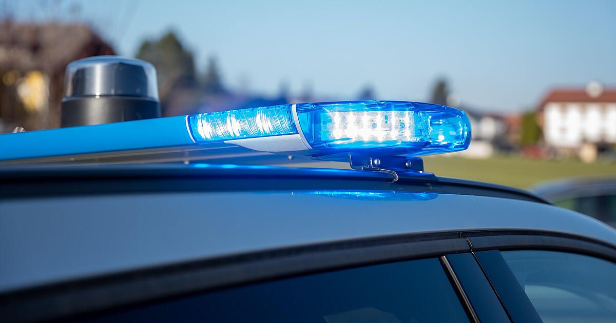Nahaufnahme eines blauen Polizeiwagens mit blinkendem blauem Licht auf dem Dach, vor einem klaren blauen Himmel.