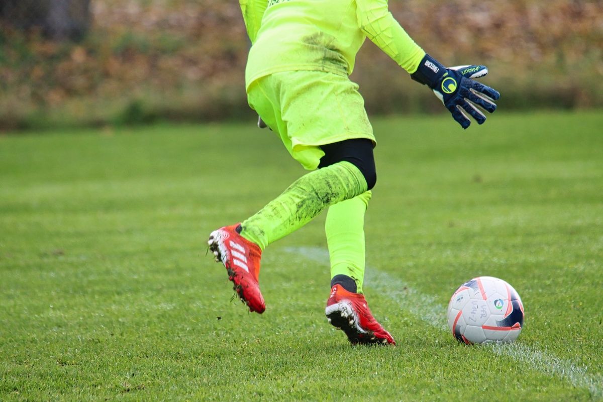Ein Fußballspieler in einem neongrünen Trikot rutscht auf dem Rasen, mit einem Fußball in der Nähe.