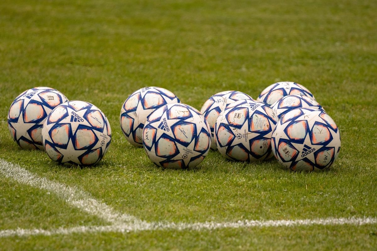 Mehrere Fußballbälle mit Adidas-Marke sind auf einem grünen Feld in einer Reihe aufgestellt, nahe einer weißen Begrenzungslinie.