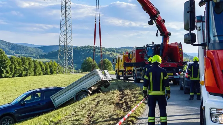 Ein Kran hebt einen beschädigten LKW in einem ländlichen Gebiet vom Boden ab, mit einem Strommast im Hintergrund.