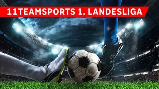 Ein Fußballspieler in blauen Socken und schwarzen Schuhen kickt einen Fußball auf einem Rasenfeld vor einem Stadion im Hintergrund.