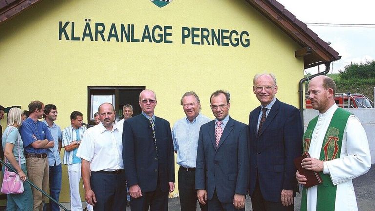Five men in suits stand in front of a yellow building with the sign 'Aranlage Pernegg' above them.