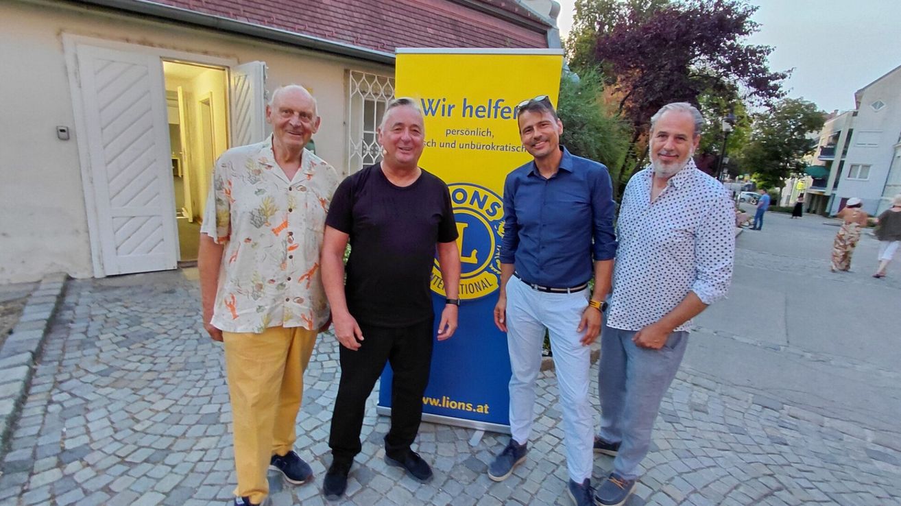 Vier Männer stehen vor einem Lions Club-Banner, lächeln und posieren für ein Foto.