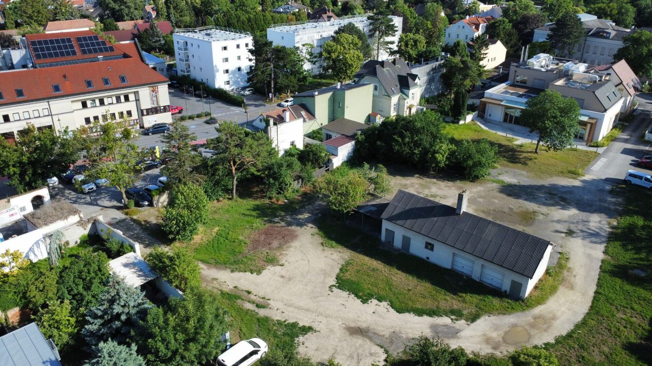 Luftaufnahme eines Vorstadtviertels mit verschiedenen Gebäuden, Bäumen und geparkten Autos. Das Gebiet umfasst eine Mischung aus Wohn- und Gewerbeimmobilien.