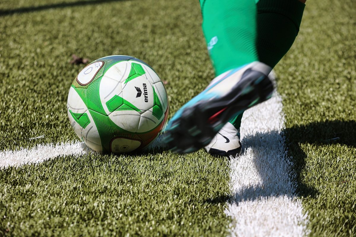 A soccer player in green uniform kicks a soccer ball with the brand name Erima on it. The ball is on the white line of the pitch.