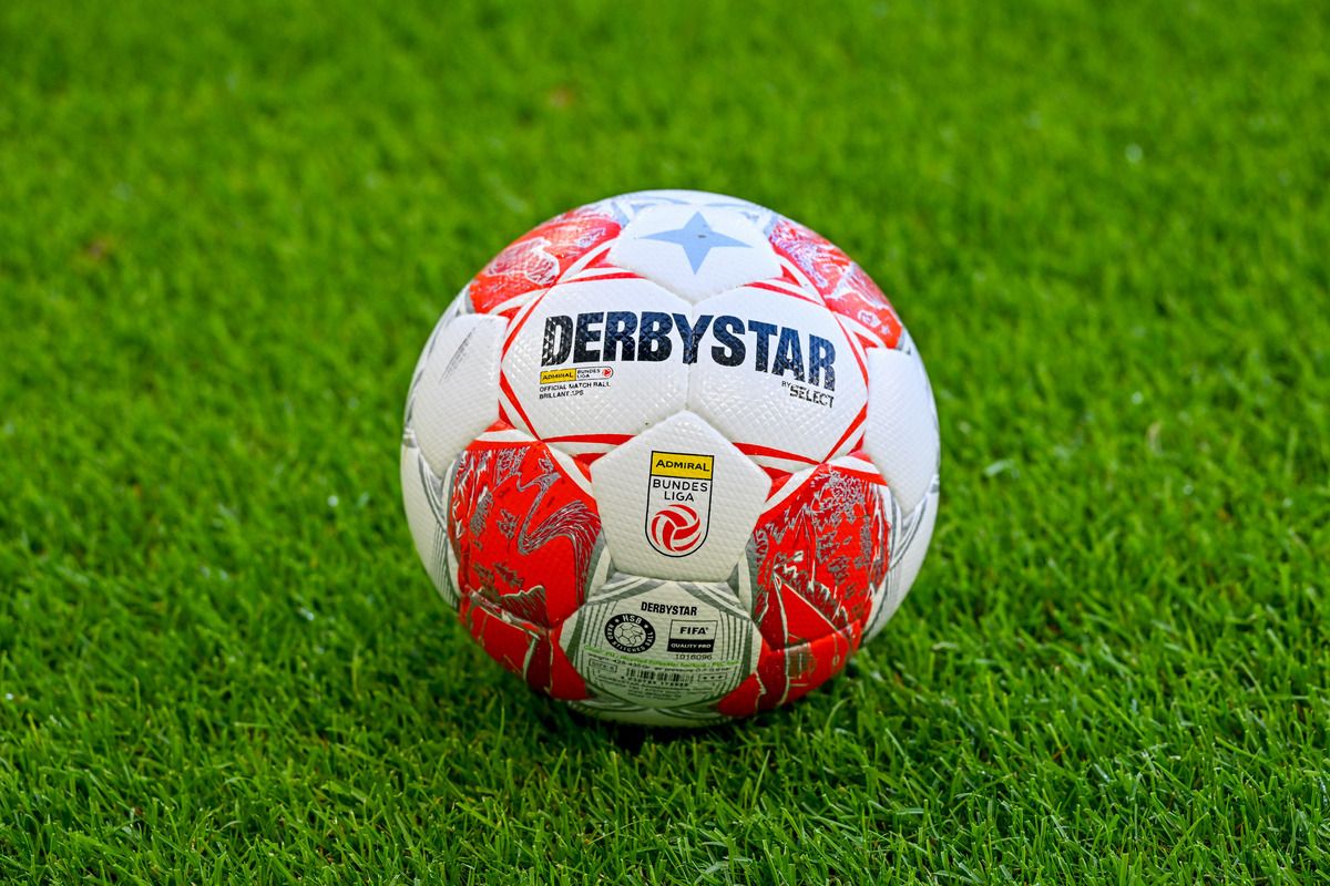 Ein rot-weißer Fußball mit dem Wort Derbystar und einem Sternlogo darauf, auf einem grünen Rasen platziert.