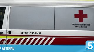 Eine Nahaufnahme der Seitenverkleidung eines Fahrzeugs mit dem Text 'Rettungsdienst' in fetten, weißen Buchstaben auf grauem Hintergrund. Darüber befindet sich ein rotes Rechteck mit dem Text 'Oster Rot'. Die Verkleidung hat einen rot-weiß gestreiften Rand.
