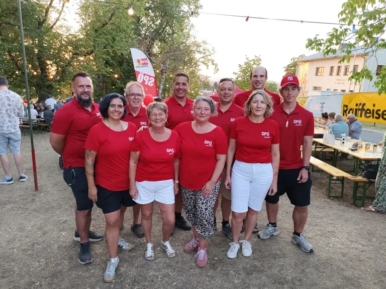 A group of people in red shirts with the letters SPO on them are posing for a photo in an outdoor setting.