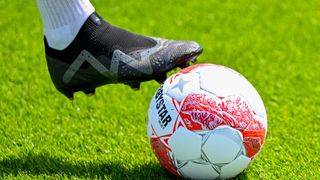 Der Fuß eines Fußballspielers in einem schwarzen Schuh steht kurz davor, einen Fußball mit rotem und weißem Design zu treten.