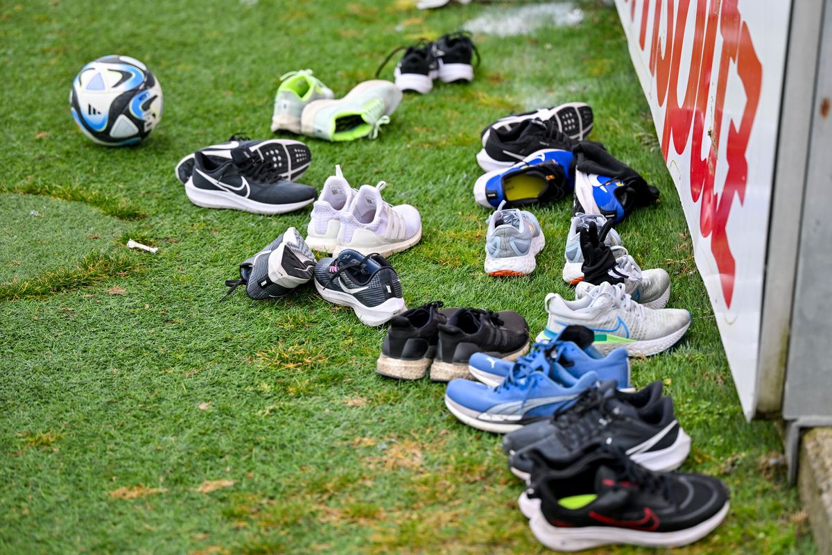 A collection of various running shoes and sports gear scattered on a grassy field. Some shoes are worn, while others are new.