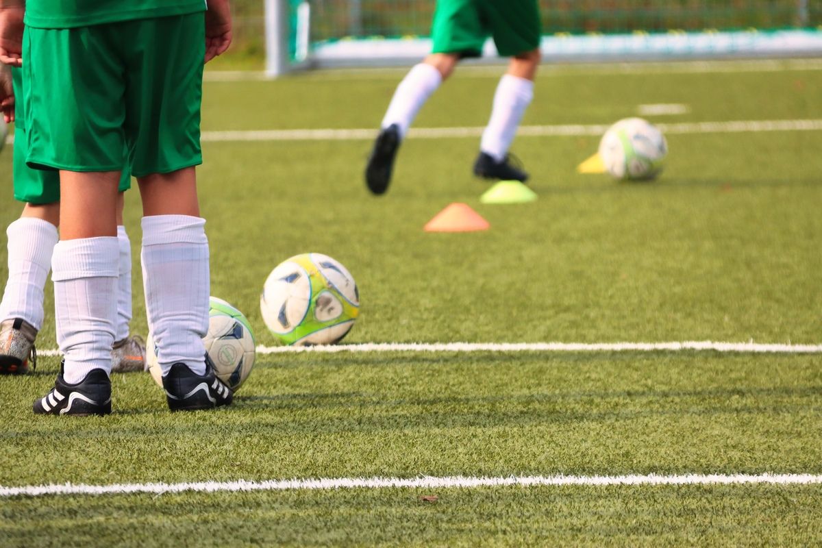 Zwei Fußballspieler in grünen Trikots stehen auf einem Feld mit Fußballbällen und Hütchen. Ein Spieler ist leicht verschwommen.