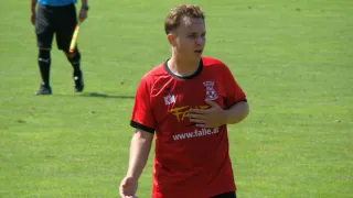Ein junger Mann in einem roten Fußballtrikot mit dem Wort 'FALL' und einer Website-Adresse steht auf einem Rasenfeld.