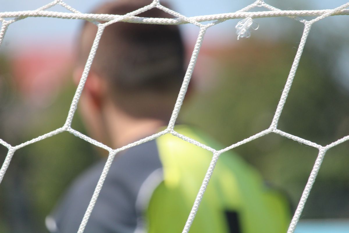 Ein Fußballspieler in einem grünen Trikot steht hinter einem weißen Netz, mit einem unscharfen Hintergrund.