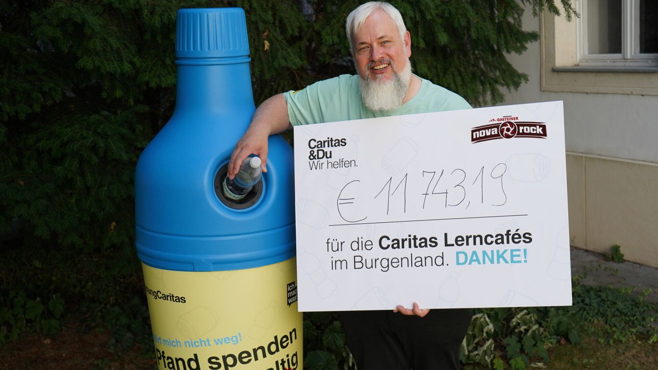 A man with a white beard holds a check for 174319 euros for Caritas in Burgenland. He stands next to a blue and yellow bottle.