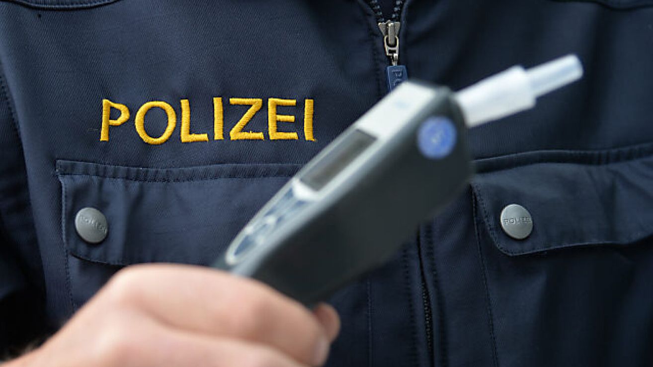 Ein Polizist hält einen Alkoholtester in der Hand, mit dem Wort 'POLIZEI' auf der Uniform aufgestickt.