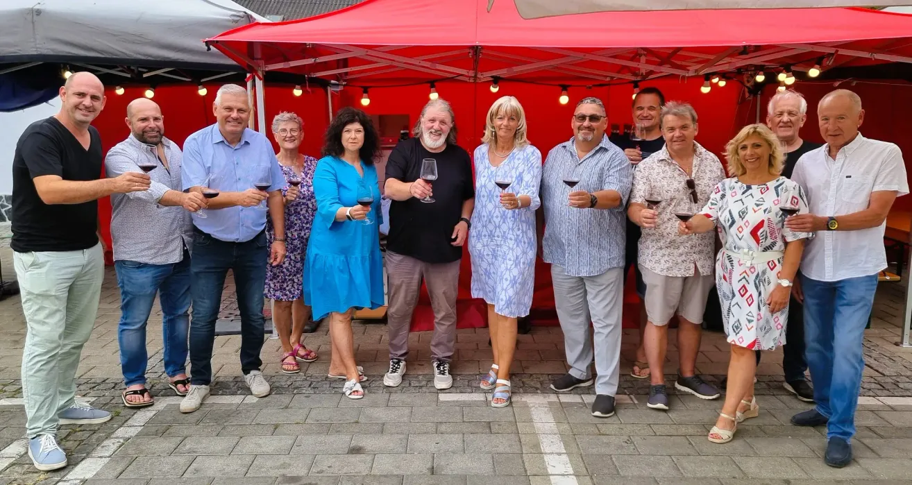 Eine Gruppe von Menschen steht unter einem roten Zelt, hält Weingläser in der Hand und lächelt für ein Foto.