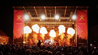 Ein nächtliches Musikfestival mit einer Bühne, die Pyrotechnik zeigt, und einer Menge von Menschen, die die Aufführung genießen.