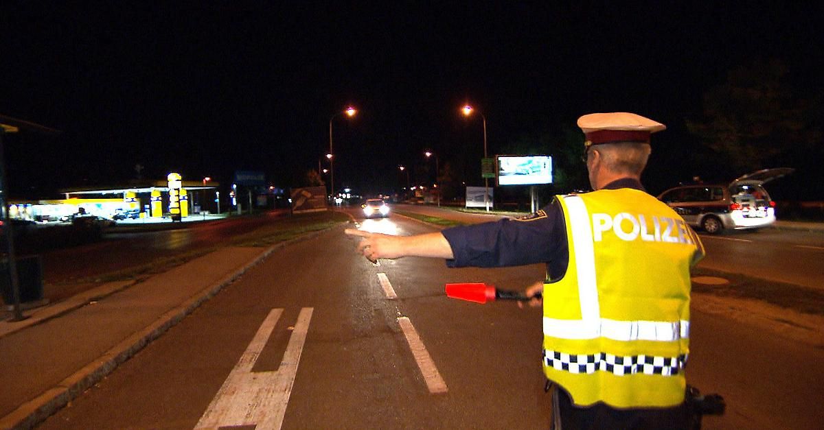 Ein Polizeibeamter in einer Warnweste zeigt auf ein Auto auf einer Straße bei Nacht.