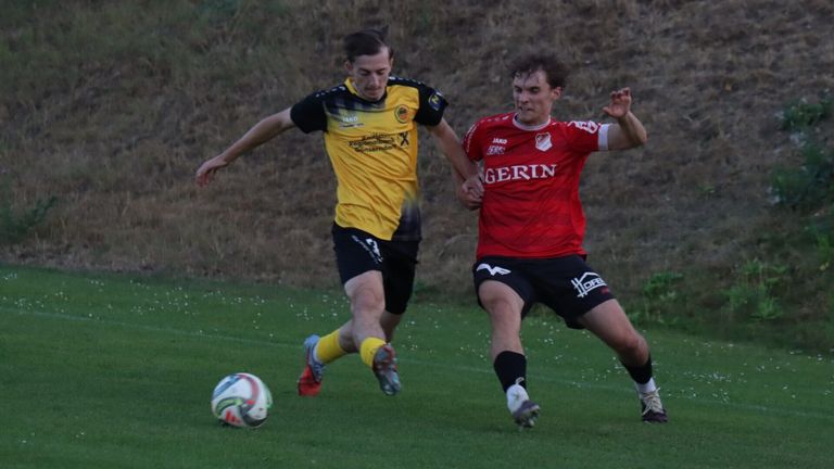 Zwei Fußballspieler, einer in einem gelben Trikot und der andere in Rot, kämpfen auf einem Rasenfeld um den Ball.