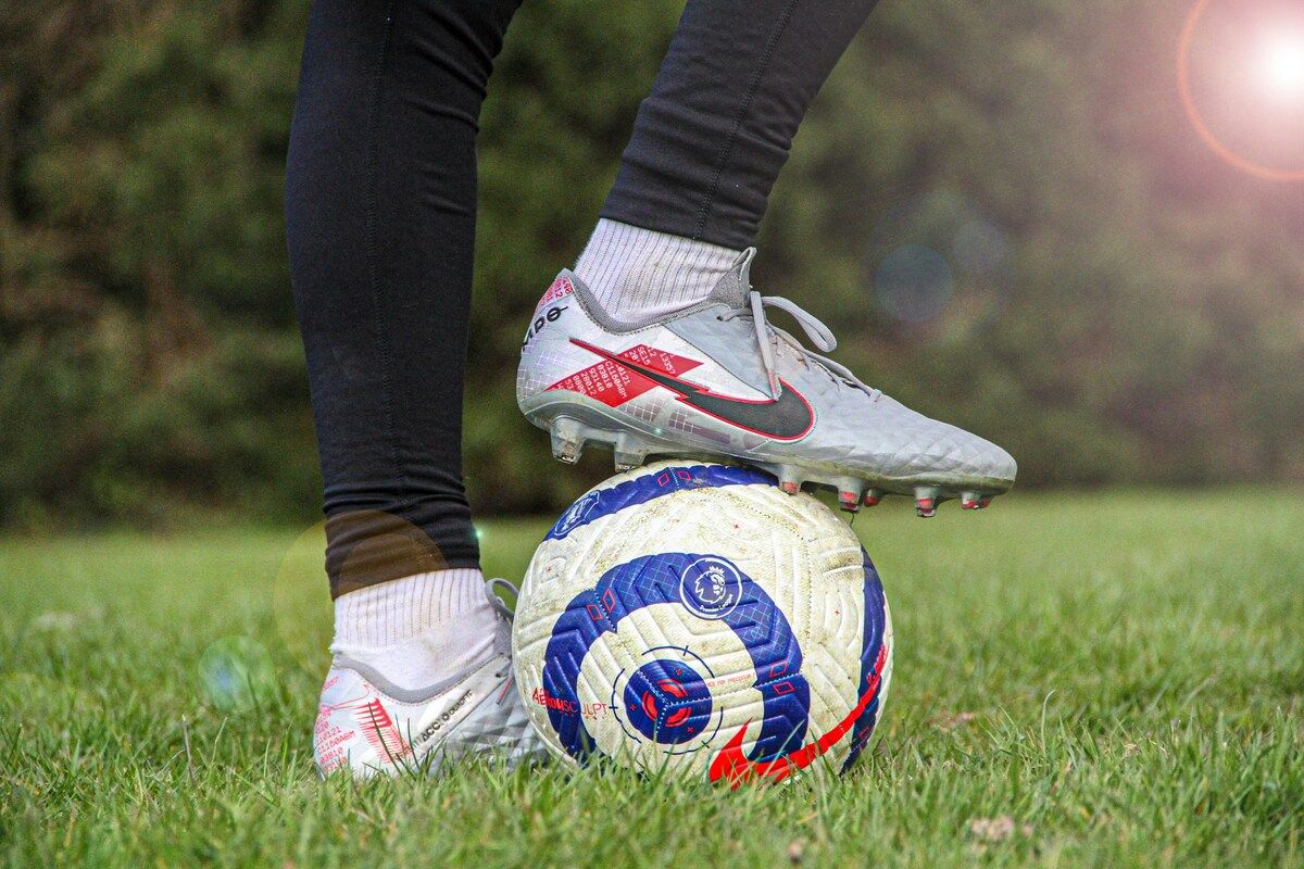 Ein Fußballspieler in schwarzen Leggings und weißen Socken steht auf einem Fußball mit einem Nike-Fußballschuh. Der Ball hat ein blaues, weißes und rotes Design.