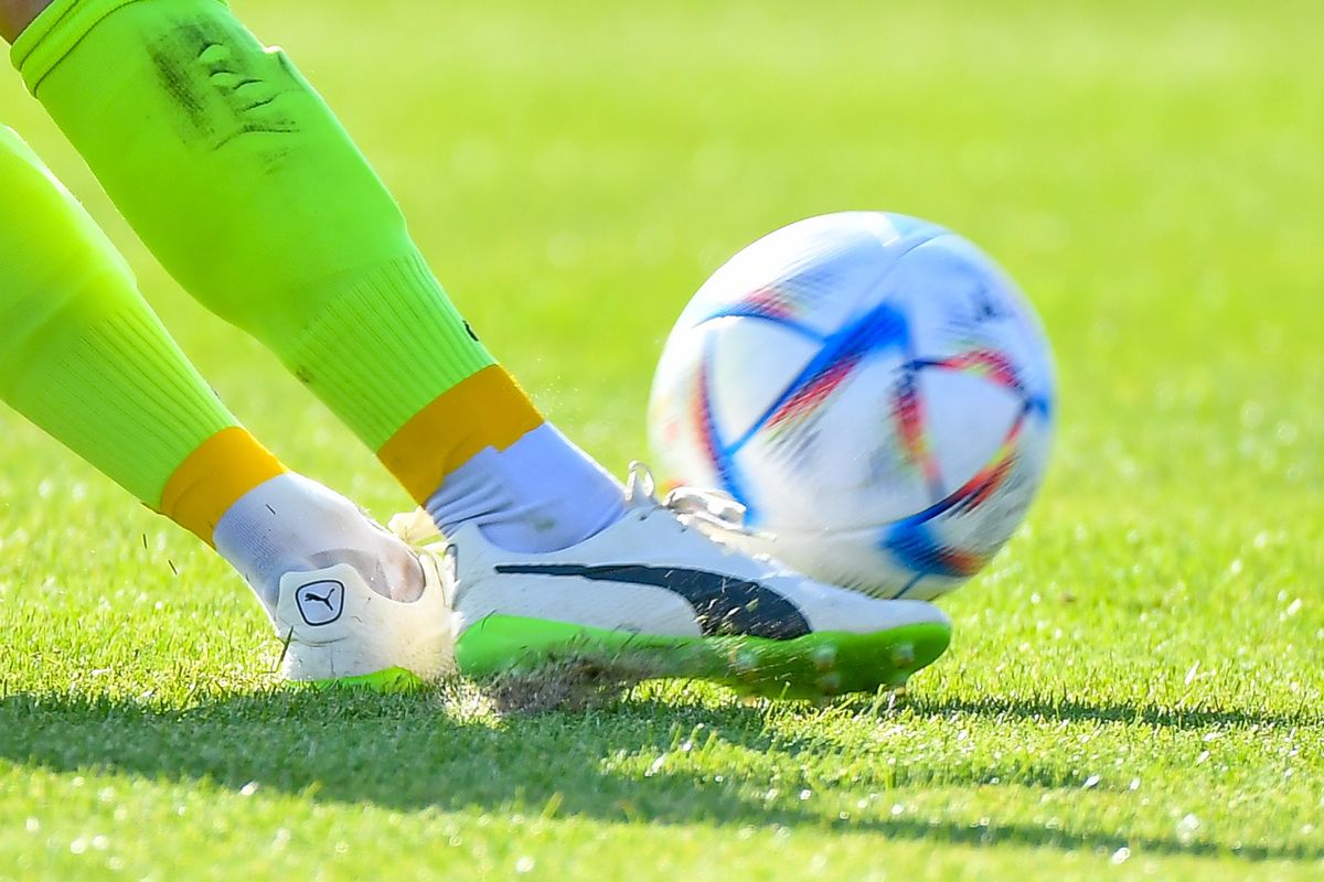 Ein Fußballspieler in grüner und gelber Ausrüstung tritt einen Fußball mit einem bunten Design auf einem Rasenfeld.