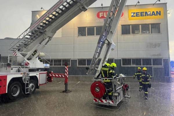 Ein Feuerwehrauto mit ausgefahrener Leiter steht vor einem Gebäude mit Zeeman-Schild. Feuerwehrleute laufen im Regen auf das Gebäude zu.
