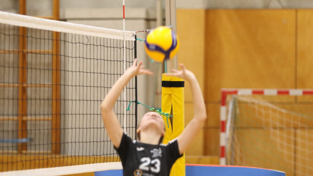 Ein junges Mädchen in einem schwarzen Trikot mit der Nummer 23 spielt Volleyball und schlägt den Ball.