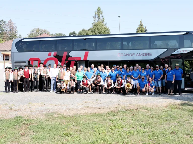 Eine Gruppe von Menschen in traditioneller Kleidung, einige mit Musikinstrumenten, posiert für ein Foto vor einem Bus mit dem Text 'Grande Amore'.