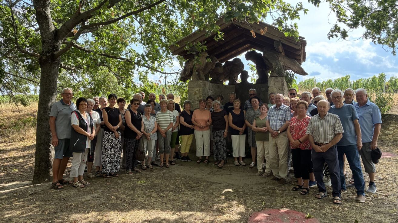 Eine Gruppe von Menschen, meist älterer, posiert für ein Foto vor einer Steinstruktur mit einer Krippe.