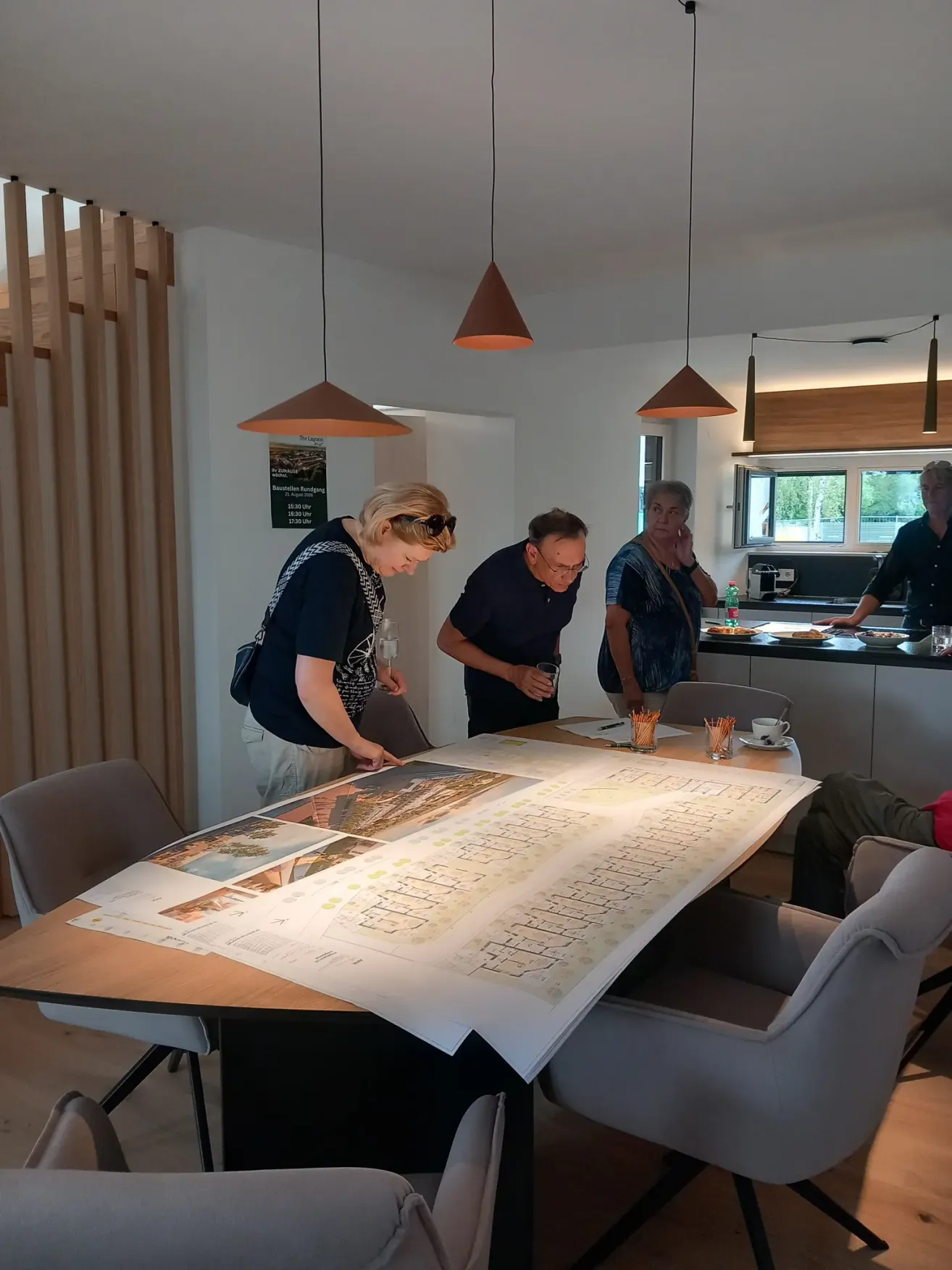Vier Personen stehen um einen Tisch mit Architekturplänen und diskutieren ein Projekt. Der Raum hat Holzakzente und moderne Beleuchtung.