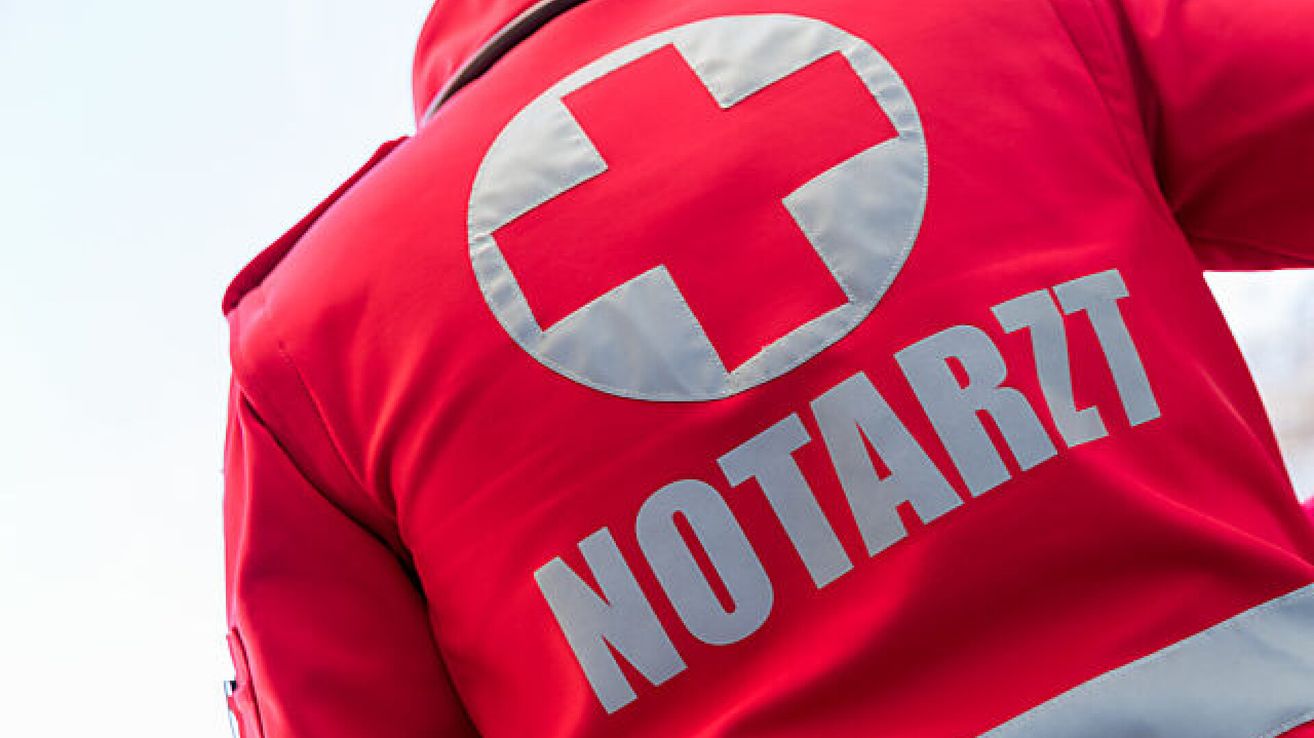 Ein Ausschnitt eines roten Jacken mit einem weißen Kreuzlogo und dem Wort 'NOTAR' in weißen Buchstaben.