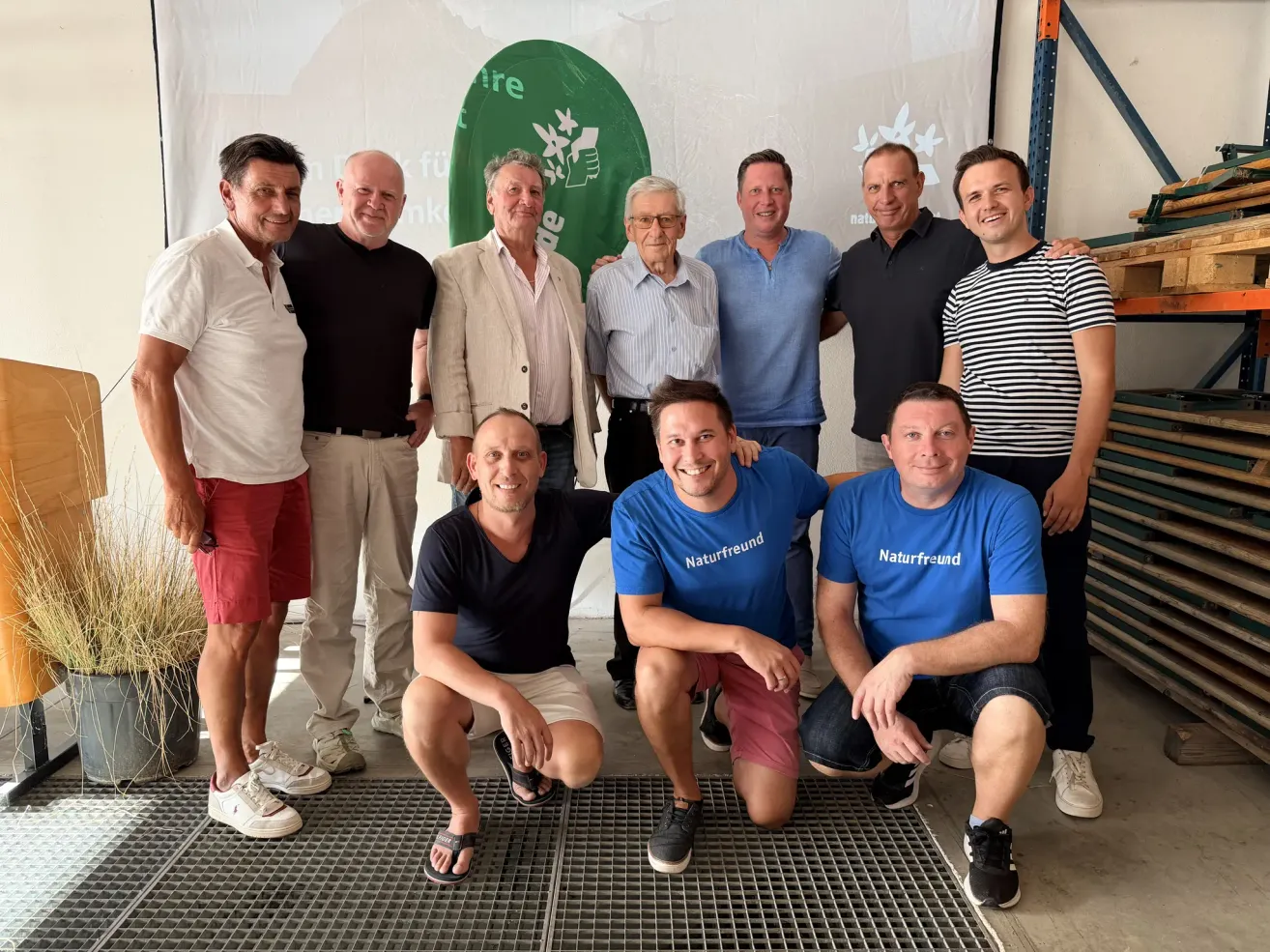 Eine Gruppe von Männern in Freizeitkleidung posiert für ein Foto vor einem weißen Hintergrund mit einem grünen Logo. Sie lächeln und scheinen für ein Teamfoto zu posieren.
