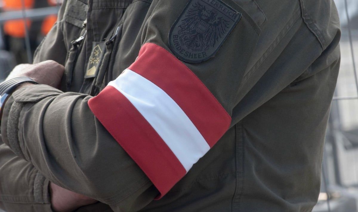 Nahaufnahme einer Militäruniform mit einem rot-weißen Armband und einem Bundesheer-Abzeichen.