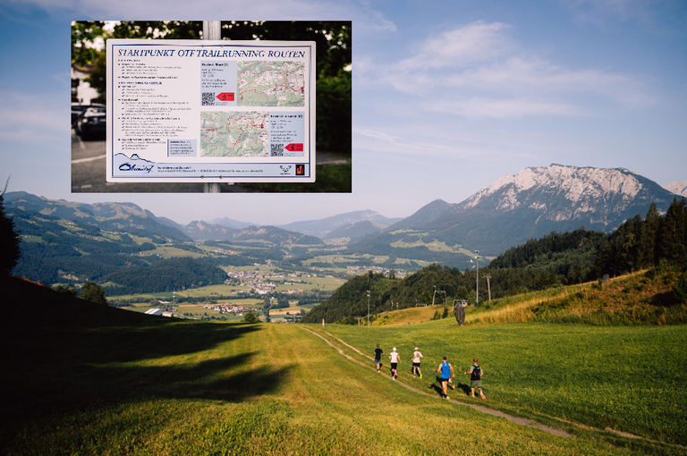 Eine Gruppe von Menschen läuft auf einem Grasweg mit einem Wegweiser im Hintergrund. Der Wegweiser steht für 'Startpunkt Off Trailrunning Roisten'. Der Weg ist von saftigem grünem Gras und Bergen in der Ferne umgeben.