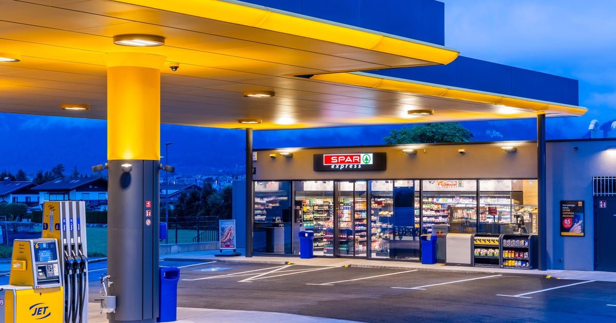 Ein Spar Express-Lebensmittelgeschäft mit Zapfsäule, beleuchtet von gelben und weißen Lichtern bei Nacht, mit einem klaren Blick auf das Innere des Geschäfts und die Produkte.