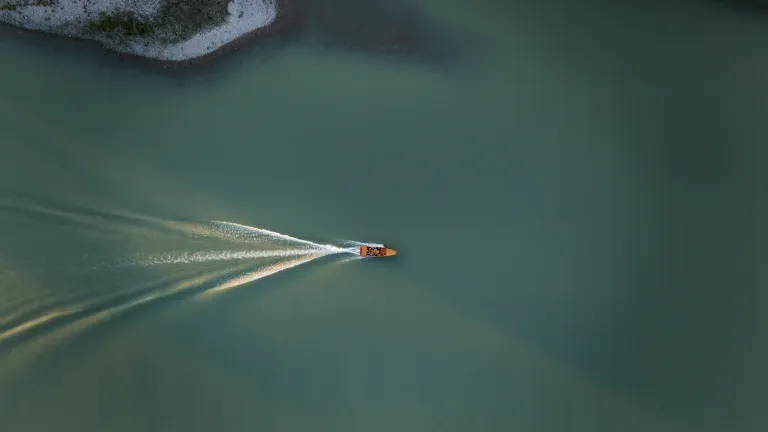 An aerial view of a small yellow boat moving swiftly on calm water, leaving a white wake behind.