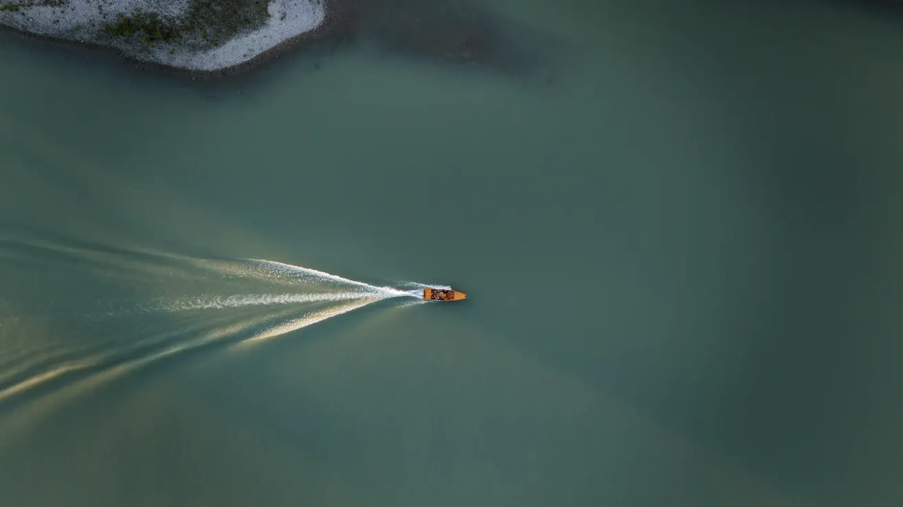An aerial view of a small yellow boat moving swiftly on calm water, leaving a white wake behind.