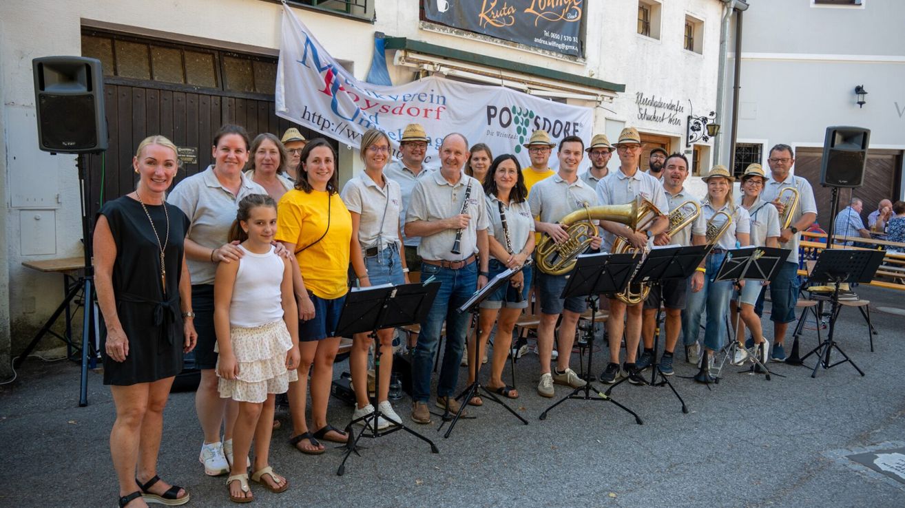 Eine Gruppe von Musikern und ihren Familien posiert für ein Foto vor einem Gebäude mit einem Banner.