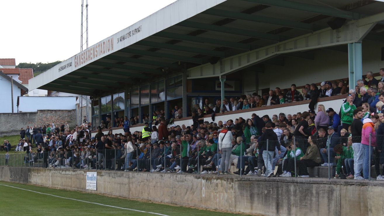 Eine große Menschenmenge, die ein Sportereignis von den Tribünen aus beobachtet, mit einem Metallzaun, der sie vom Spielfeld trennt.