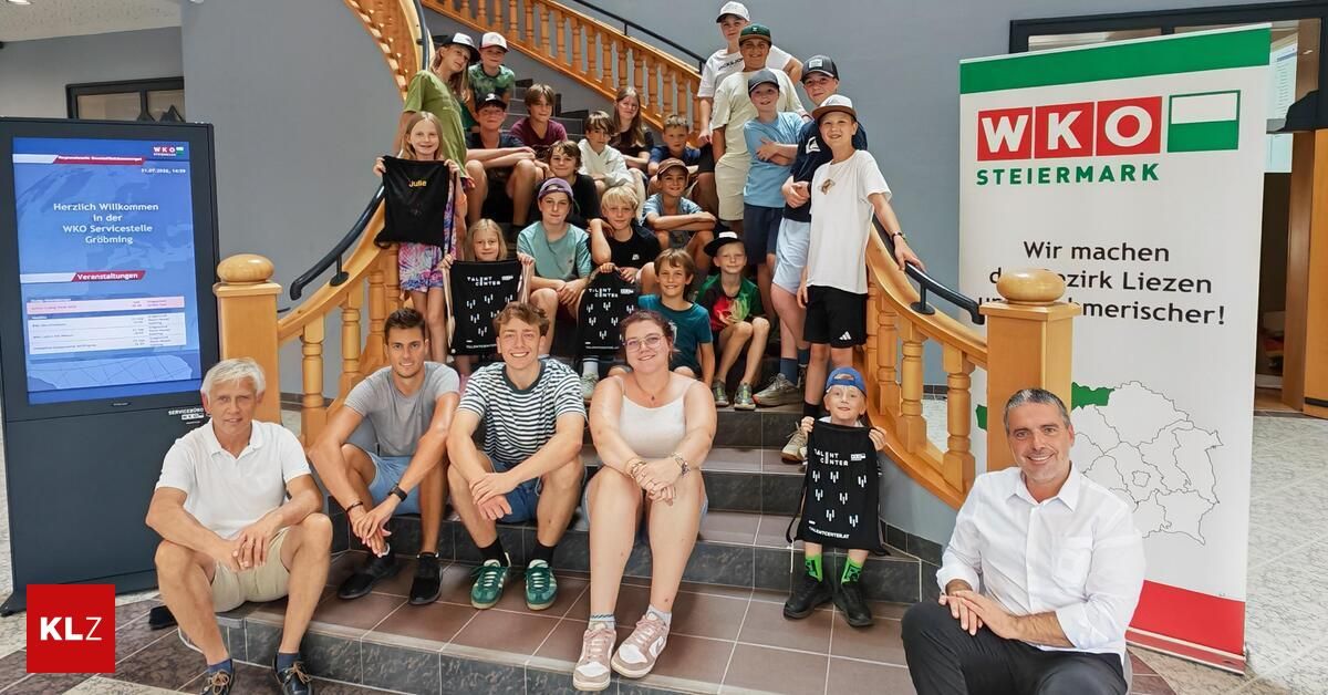 Eine Gruppe von Menschen, einschließlich Kindern und Erwachsenen, posiert für ein Foto auf einer Treppe. Sie tragen alle Mützen und einige halten Taschen. Die Treppe hat Holzgeländer. Ein Schild mit dem Text 'WK STEIER' befindet sich auf der rechten Seite.