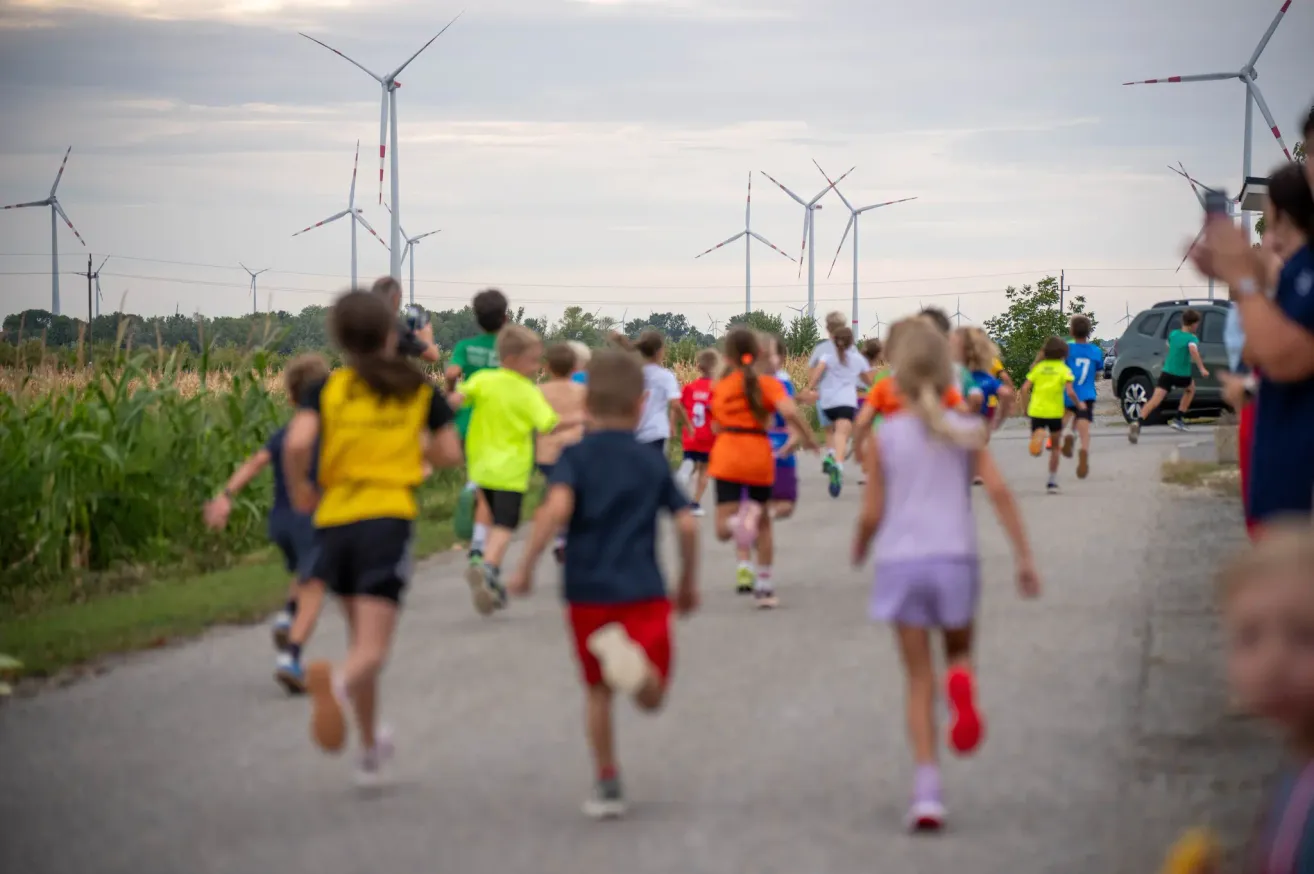 Eine Gruppe von Kindern in Sportkleidung, die an einem Rennen teilnehmen, mit Windturbinen im Hintergrund.
