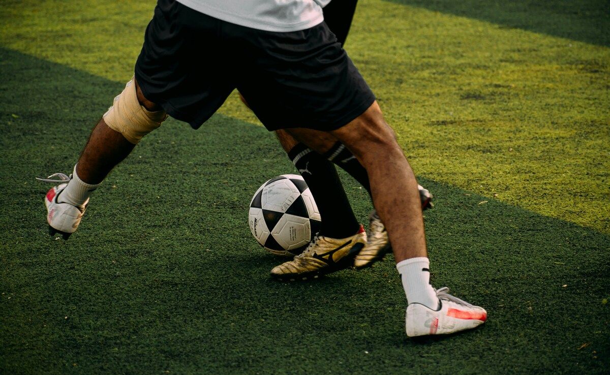 Ein Fußballspieler in schwarzen Shorts und Socken mit goldenen Schuhen steht kurz davor, einen Fußball auf einem grünen Feld zu schießen.