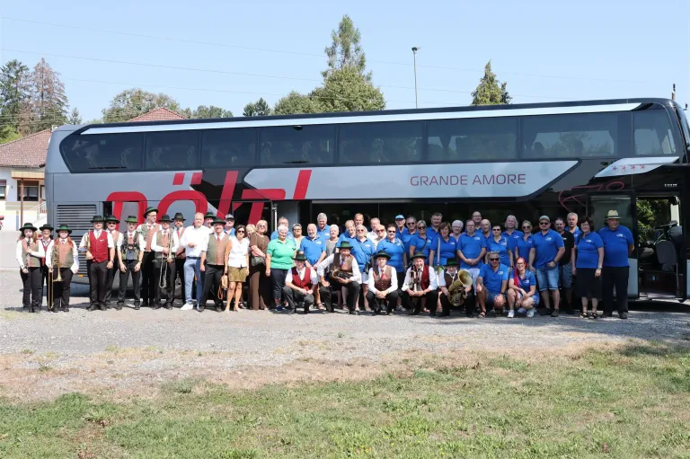Eine Gruppe von Menschen in traditioneller Kleidung, einschließlich Hüten und Westen, posiert für ein Foto vor einem Bus namens Grande Amore.