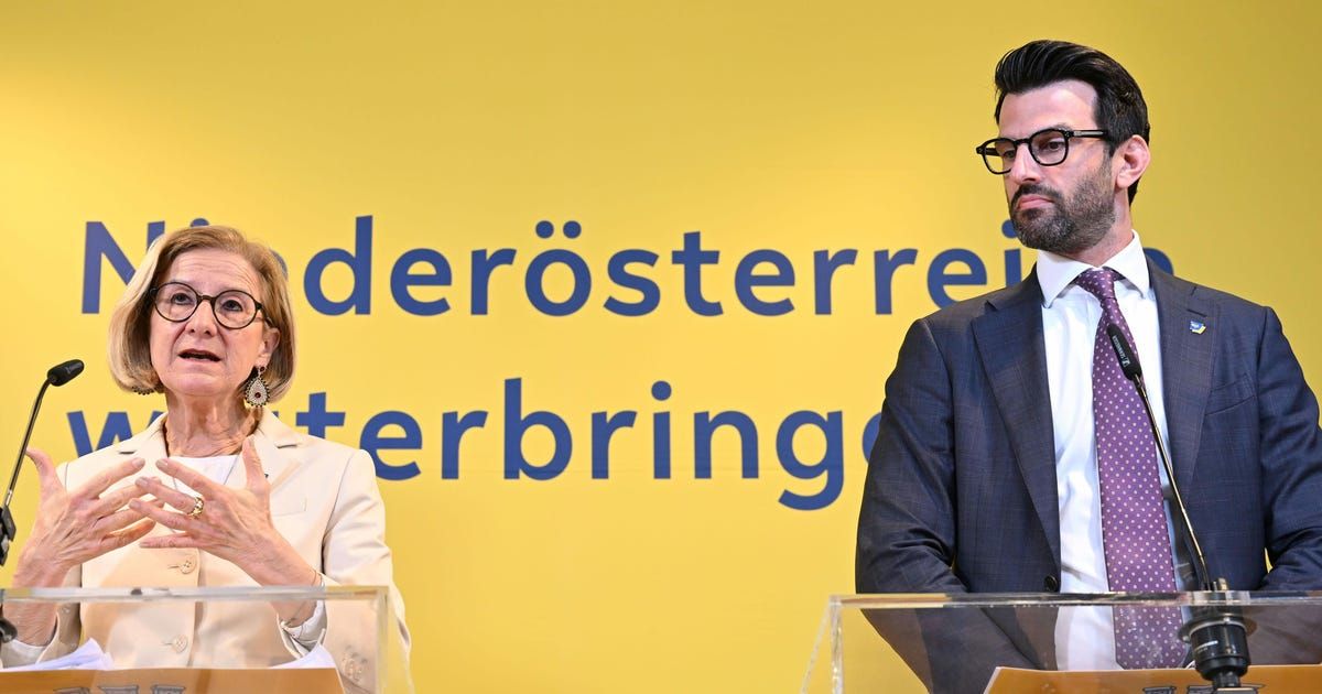 A man and a woman stand at podiums in front of a yellow backdrop with blue text reading 'derösterrein' and 'terbringen'. The woman holds a microphone and speaks, while the man looks on.