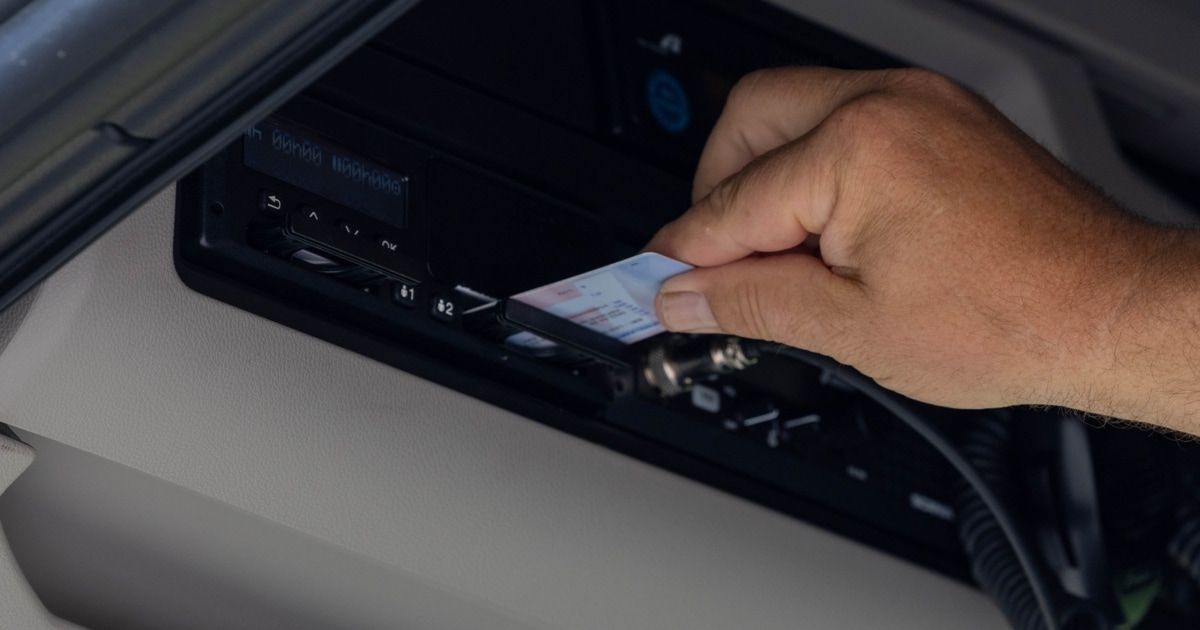 Eine Hand steckt eine Karte in das elektronische Zahlungssystem eines Fahrzeugs, wobei ein digitales Display Zahlen und Symbole anzeigt.